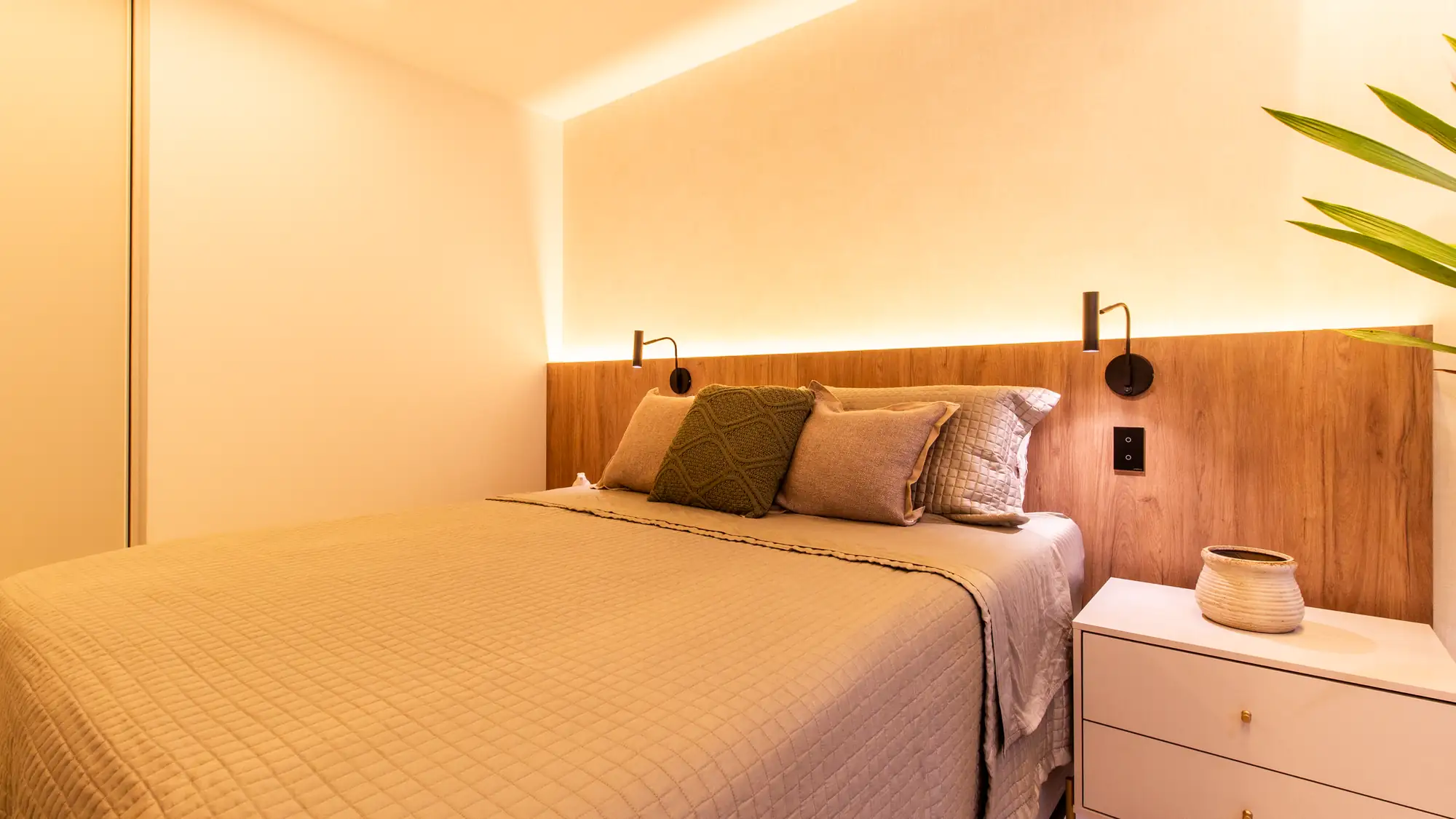 Quarto: Cabeceira em madeira de parede inteira com luz indireta.